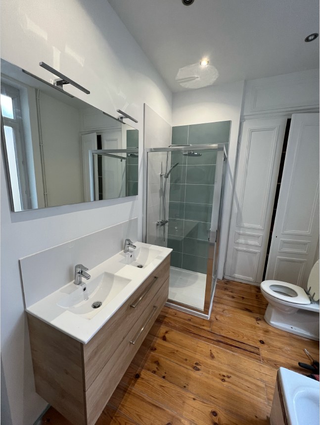 Salle de bain rénovée avec meuble double vasque en bois et douche carrelée vert sauge — HFE Lille